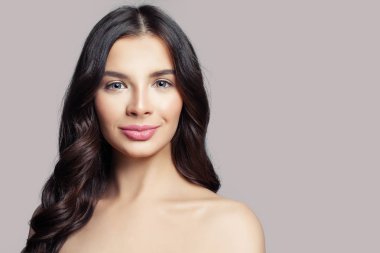 Güzel bir kadın yüzü. Uzun kıvırcık saçlı pembe bir arka plan üzerinde gülümseyen kadın modeli