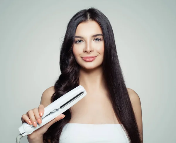 Beautiful woman with straight hair and curly hair using hair straightener. Cute girl straightening healthy hair with flat iron. Hair care concept