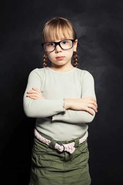 Cute child in glasses thinking against school classroom blackboad — Stock Photo, Image