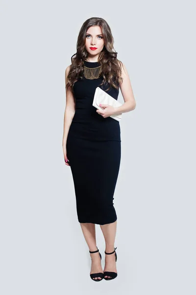 Elegancka modelka kobieta ubrana w czarną sukienkę stojącą przed białą ścianą — Zdjęcie stockowe