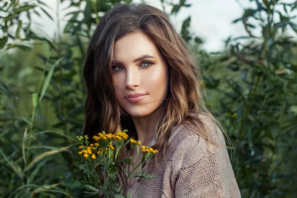 夏の緑の草に黄色い日焼けした花を持つ笑顔の女性 — ストック写真