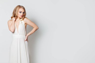 Beyaz duvara karşı beyaz gece elbisesi giyen güzel kadın 