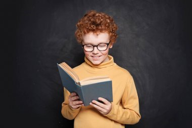 Tebeşir tahtası arka planı yla ilgili bir kitap okuyan çocuk. Sevimli çocuk çocuk
