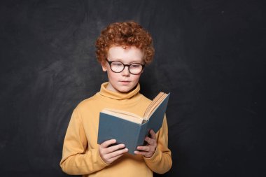 Çocuk tahta arka plan üzerinde bir kitap okuyor. Sevimli küçük çocuk 