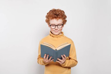 Gözlüklü çocuk beyaz arka plan üzerine bir kitap okuyor