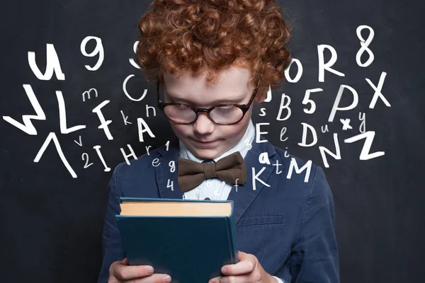 Rotschopf-Kind mit Buch auf Schultafel Hintergrund — Stockfoto