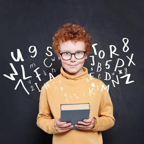 Bambino ragazzo tenendo libro su sfondo lavagna con lettere — Foto Stock