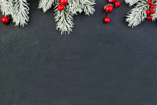 Black Christmas background with snowy Xmas tree twig and red holly berries — Stock Photo, Image