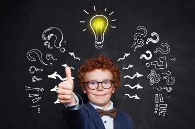 Sevimli çocuk tahta arka plan üzerinde ampul ile başparmak tutarak