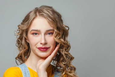 Sarı saçlı ve gri arka planda sağlıklı ciltli güzel bir genç kadın.