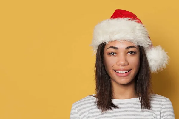 Happy smiling black woman in Santa hat on yellow background