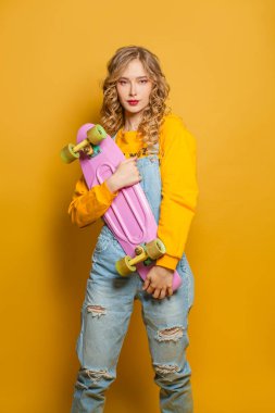 Sarı kazaklı hoş bir kadın arka planda kaykay tutuyor.