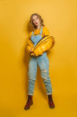 Sarı kışlık ceketli güzel manken kadın parlak arka planda duruyor.