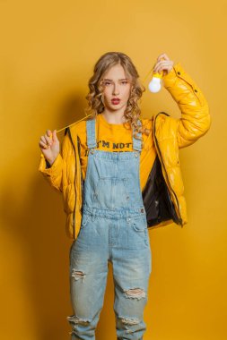 Sarı kazaklı genç bir kadın sarı arka planda ampul tutuyor.