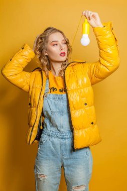 Moda kızı sarı arka planda ampul tutuyor.