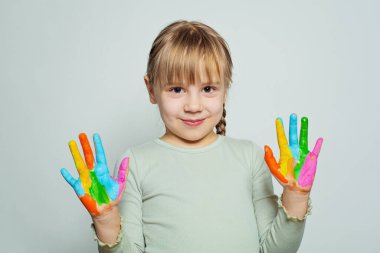 Sevimli mutlu çocuk sanat okulu öğrencisi renkli boyalı ellerini beyaza gösteriyor. Kız çizimi