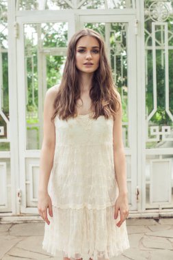 Bahçede duran beyaz elbiseli genç kadın.