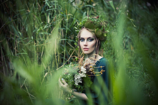 Beautiful fairy witch woman in green grass outdoors. Halloween character or Forest soul