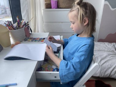 Masasında boş bir eskiz defteri olan ciddi bir kız çocuğu. Ev hayatı, boş zaman aktivitesi.