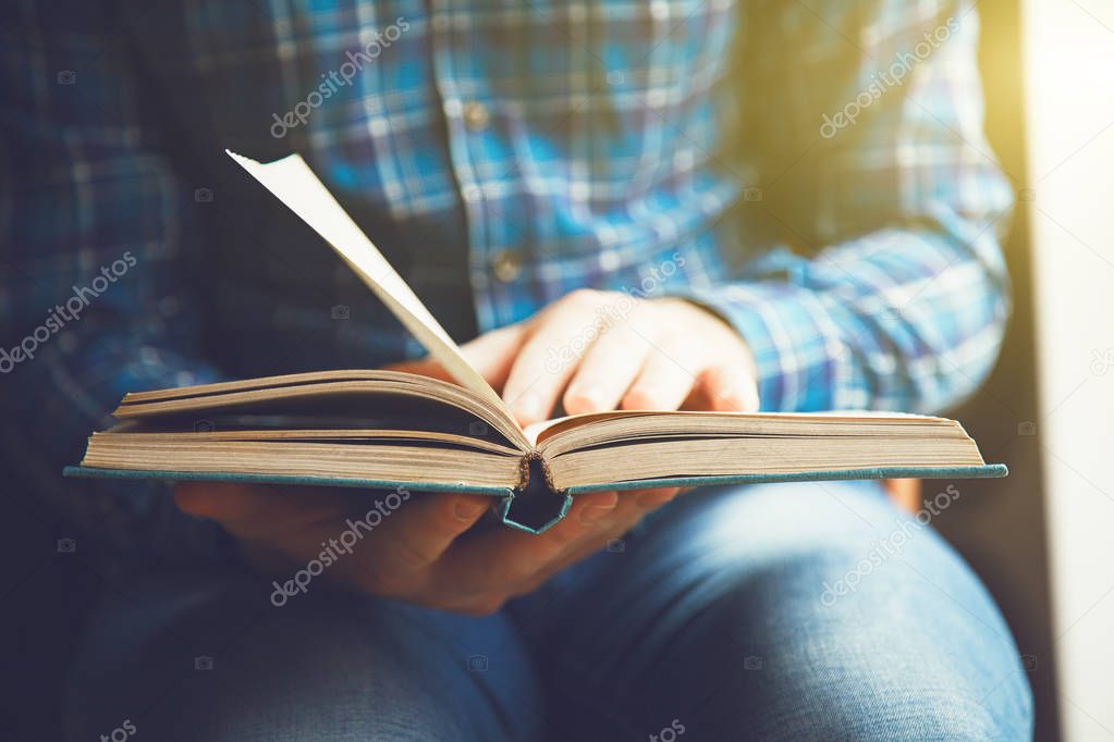 Partial view of man sitting on chair reading book