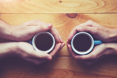 Hands of couple with two cups of coffee on wooden table, elevated view clipart