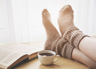 Sabah kahve masada sıcak çorap tutma bacaklar dinlenme ve kitap okuma kadın