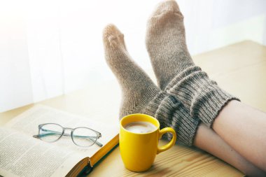 Sabah kahve masada sıcak çorap tutma bacaklar dinlenme ve kitap okuma kadın