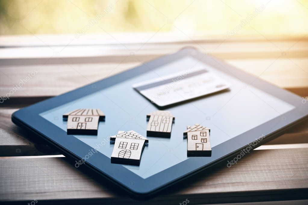 Wooden symbols of houses and credit card on digital tablet computer.  Online house choosing or rental of property concept
