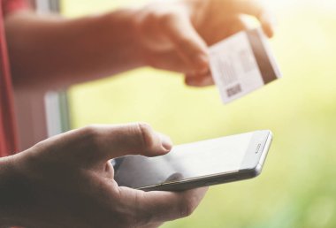 Kredi kartı tutan ve akıllı telefon kullanan eller. İnternetten alışveriş