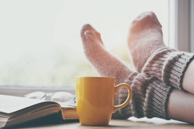 Sabah kahve masada sıcak çorap tutma bacaklar dinlenme ve kitap okuma kadın