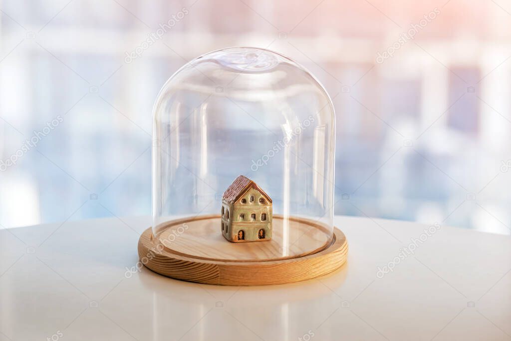 Ceramic model of house under glass cap. Symbol of safe home. Insurance or protecting building property concept. 