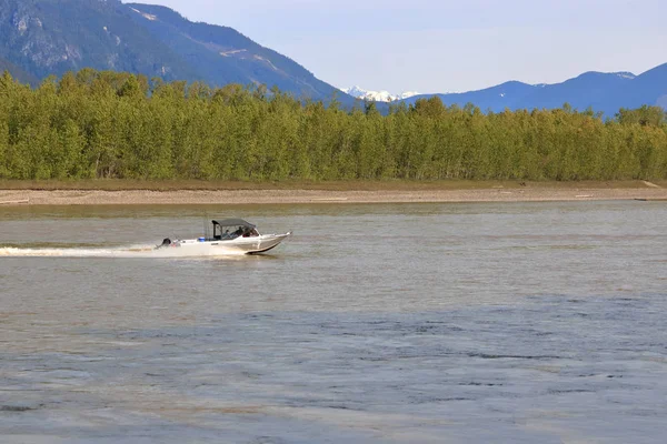 A recreational fishing boat speeds from left to right across the river water with mountains in the background.