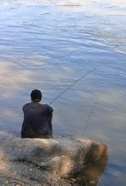 一个人坐在水边钓鱼杆的垂直视图 — 图库照片