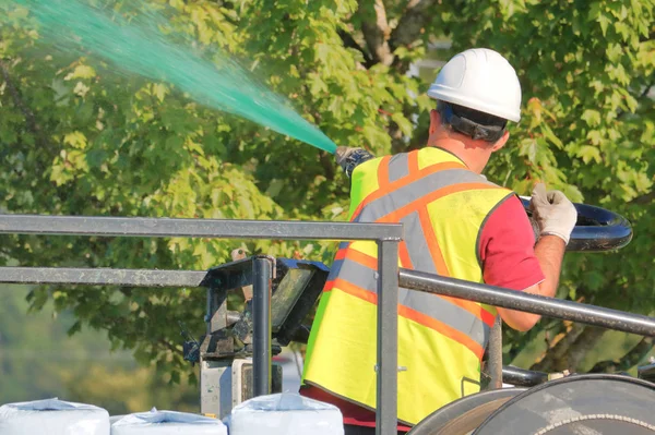 一名工人使用高压软管将绿色液体肥料传播到城市植物和树木 — 图库照片