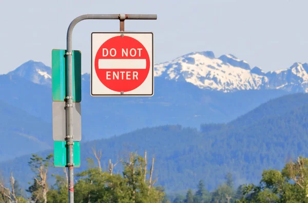 An English sign states do not enter with beautiful snow capped mountains in the background.