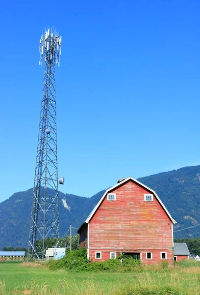 收音机和固定电话时代建造的红色谷仓的正面垂直视图矗立在现代高速传输塔前 — 图库照片