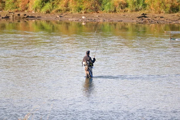 当一个男人站在清澈的淡水河里用他的钓竿和钓丝钓鱼时 他穿着草裙 目光远大 — 图库照片