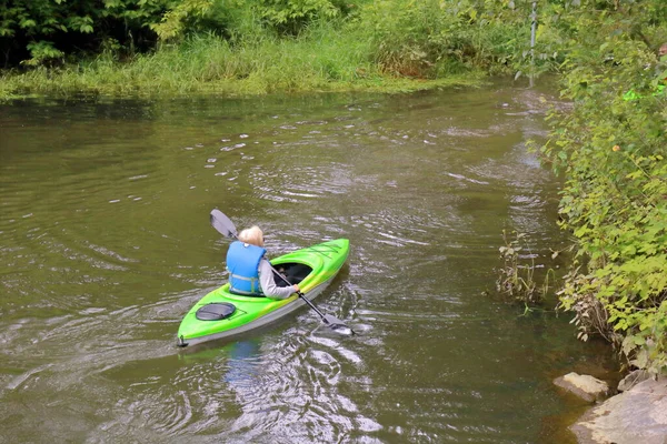 一位年长的女性划着独坐的皮划艇在平静浅浅的水面上划着 四周环绕着大自然 — 图库照片