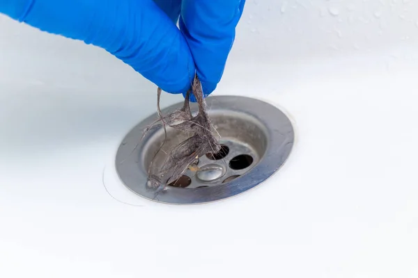 hand in glove cleaning a clogged sink or bathtub drain from hair