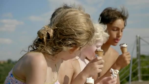 一个女孩和三个男孩坐在长椅上的海滩上吃冰淇淋在一个晴朗的日子 — 图库视频影像