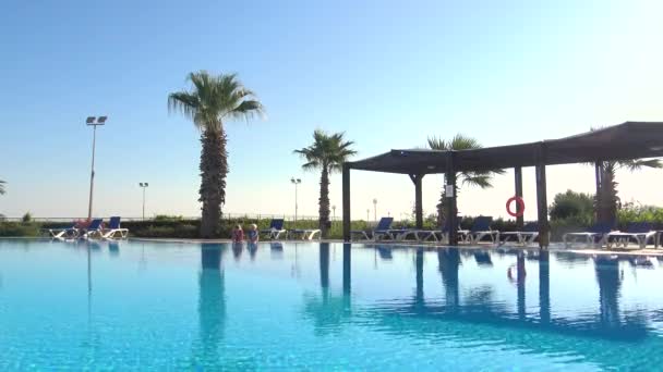 Dos niños sentados al borde de la piscina en un día soleado — Vídeo de stock