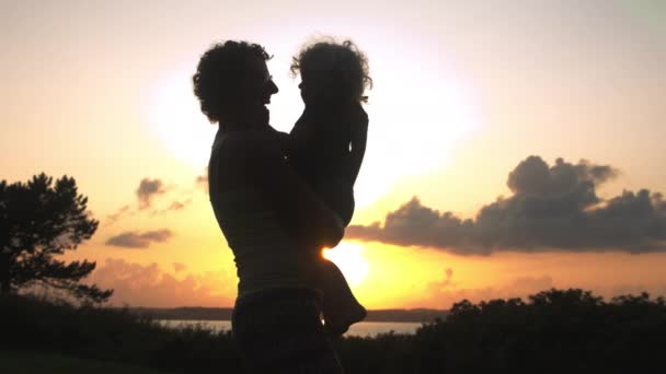 Silhouet van een gelukkige moeder die haar zoon in haar armen draagt in slow-motion — Stockvideo