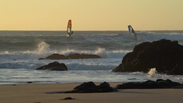Focused Shot of Two Sailboarders Riding the Waves Crashing on a Rocky Beach — Stock Video