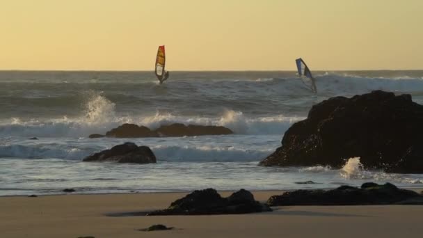 Terfokus Shot of Two Sailboard Riding the Waves Crashing on a Rocky Beach — Stok Video