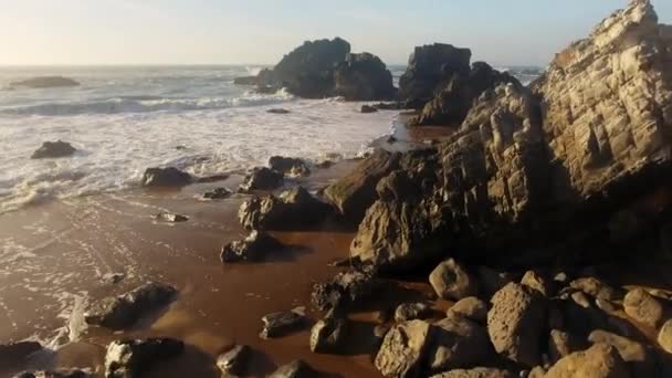 Tracking Shot of a Rocky Beach with Rough Waves Crashing on a Reddish Sand — Wideo stockowe