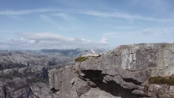 Schwenkaufnahme eines Touristen, der am Kanzelfelsen sitzt und die Aussicht bewundert, Norwegen — Stockvideo