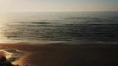 Arka planda güneş ışığı olan Danimarka sahillerinde sörf yapan bir adamın fotoğrafı.