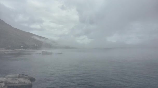 Montagne e acque oceaniche sulla riva ricoperte da nebbia spessa — Video Stock