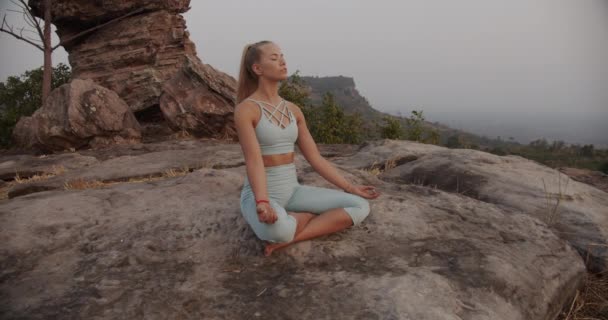 Blondýny žena v lotosové józe pozice na vrcholu hory a skály v pozadí — Stock video