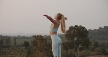 Güzel sarışın kadın ellerini başının üstüne uzatıyor ve dışarıda yoga yapıyor.